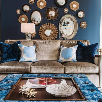 Elegant living room with mirrored wall accents, plush sofa, blue velvet pillows, and decorative elements on a modern coffee table.